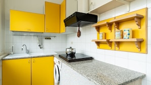 Uma cozinha com armários amarelos, um exaustor preto, bancada de granito e uma máquina de lavar.