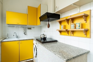 Una cocina con armarios amarillos, una campana extractora negra, encimera de granito y una lavadora.