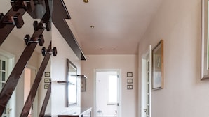 Um interior moderno com escadas, um corredor que leva a uma porta e quadros nas paredes.