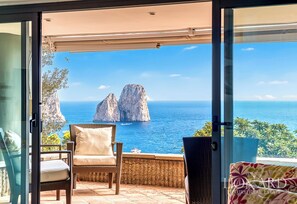 A balcony with wicker chairs and a view of the sea and rocky formations. - Villa Sirenella (Capri)