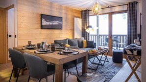 Una habitación acogedora con una mesa de madera para cuatro personas, un sofá y un balcón con mobiliario de exterior.