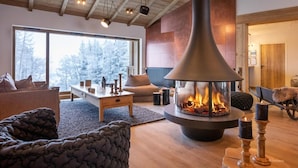 A cozy living room with a large fireplace, wooden furniture, and a view of snow-covered trees through large windows. - Wifi, 10m from ski slopes, view mountain, swimming pool, sauna, hammam, balcony, parking, ski locker (Aime)
