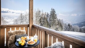 Une terrasse en bois avec une table dressée pour le petit-déjeuner, offrant une vue sur un paysage montagneux enneigé.