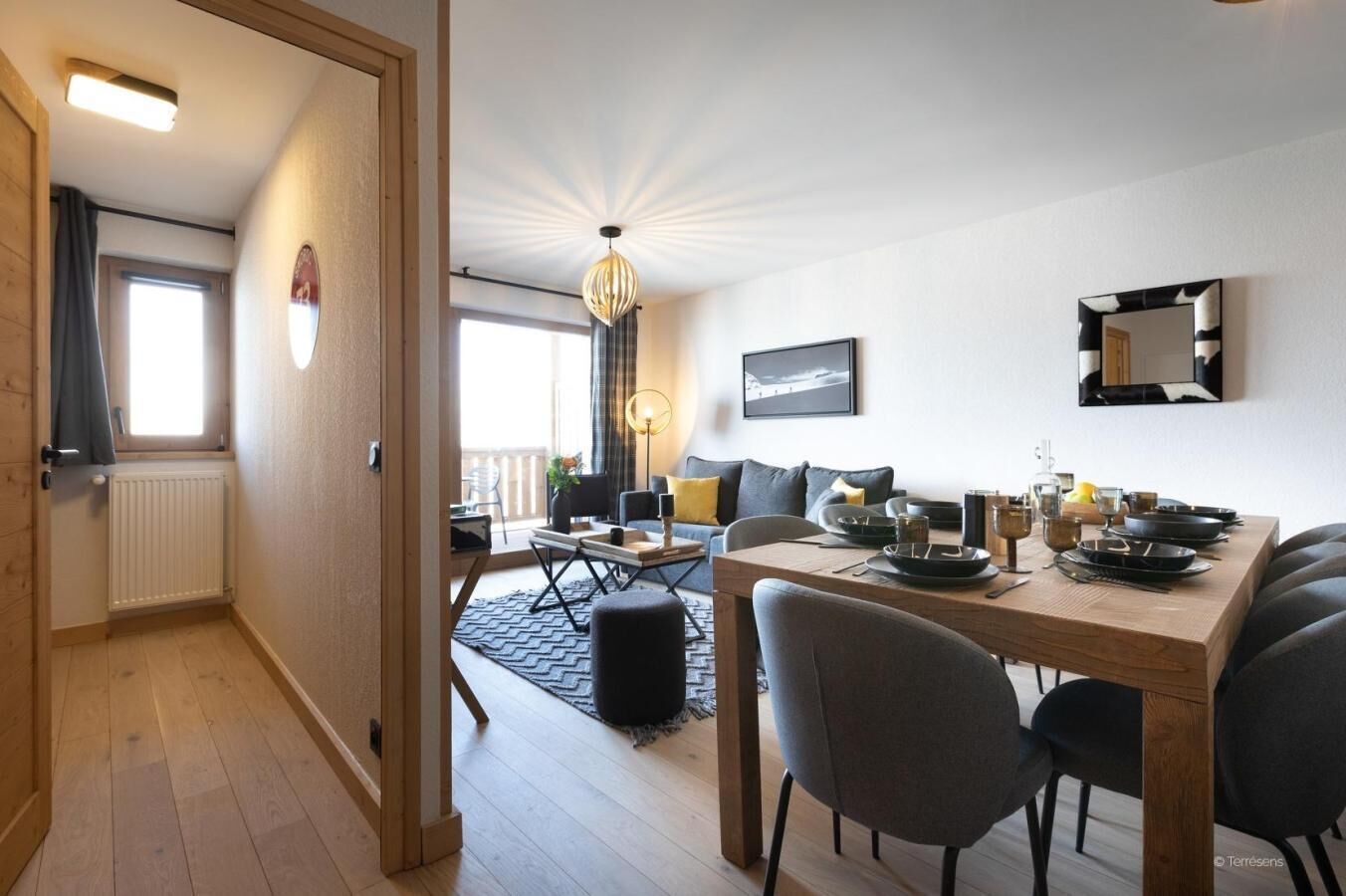 Ein modernes Wohnzimmer mit Essbereich, ausgestattet mit einem Holzesstisch für vier Personen, einer Couch und einem großen Fenster, das natürliches Licht hereinlässt.