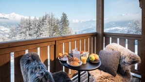 Ein Balkon mit einem für das Frühstück gedecktem Tisch, mit Blick auf eine verschneite Berglandschaft.