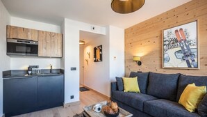 En moderne opholdsstue med et køkken, en grå sofa med gule puder og et sofabord med croissanter.
