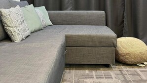 A modern living room with a grey sectional sofa, a woven pouf, and a patterned rug.