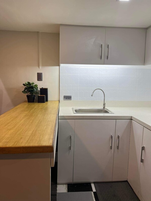 A modern kitchen with a wooden countertop, white cabinets, a sink, and a potted plant.