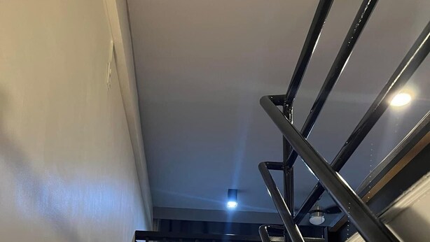 A staircase with wooden steps and a metal handrail, leading to a landing with a dark curtain backdrop.