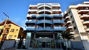 A multi-story hotel with a modern design, featuring balconies on each floor and a central entrance with glass doors. - Apto. Amplo, à 200 mts da Bela Praia do Forte e 2 Vagas de Garagem (Algodoal Cabo Frio)