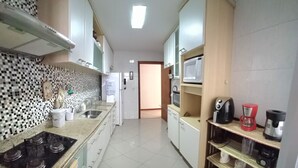 A kitchen with a tiled backsplash, a stove, a microwave, and various appliances on the countertops. - Apto. Amplo, à 200 mts da Bela Praia do Forte e 2 Vagas de Garagem (Algodoal Cabo Frio)