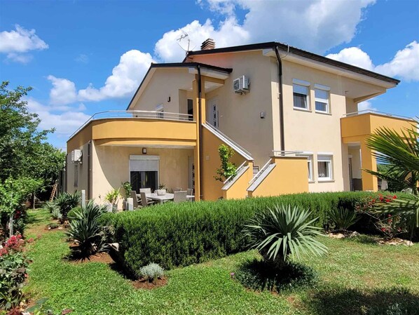 A two-story house with a balcony, a staircase, and a garden with various plants.