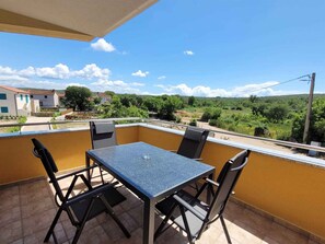 A balcony with a table and chairs, overlooking a rural landscape with houses and greenery.