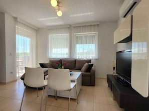 A living room with a sofa, two chairs, a TV, and a dining table.