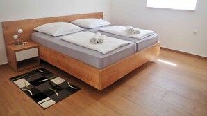 Un lit double avec une tête de lit en bois, deux tables de chevet, un tapis noir et blanc et une fenêtre avec des stores.