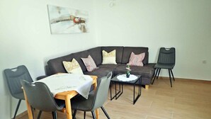 Un salon moderne avec un canapé d’angle, une table à manger avec des chaises et une petite table d’appoint sur laquelle est posée une plante en pot.