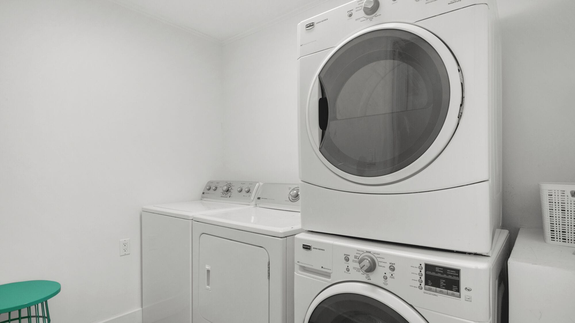 A laundry room with stacked washers and dryers, a green table, and a white wall.