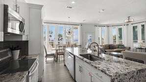 A modern kitchen with a large island, a dining area with a view, and a living area with a sofa and table. - Gulf-front, Private Pool ~ Stunning Gulf Views From All Levels + Beach Setup (Panama City Beach)