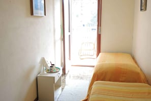 Une chambre avec un lit, une petite table avec une lampe, une chaise devant la porte et une vue sur l’extérieur.