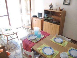 Un coin repas avec une table dressée pour quatre personnes, un téléviseur posé sur un meuble en bois et une fenêtre offrant une vue agréable.
