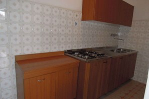 A kitchen with a stove, sink, wooden cabinets, and patterned tiles.