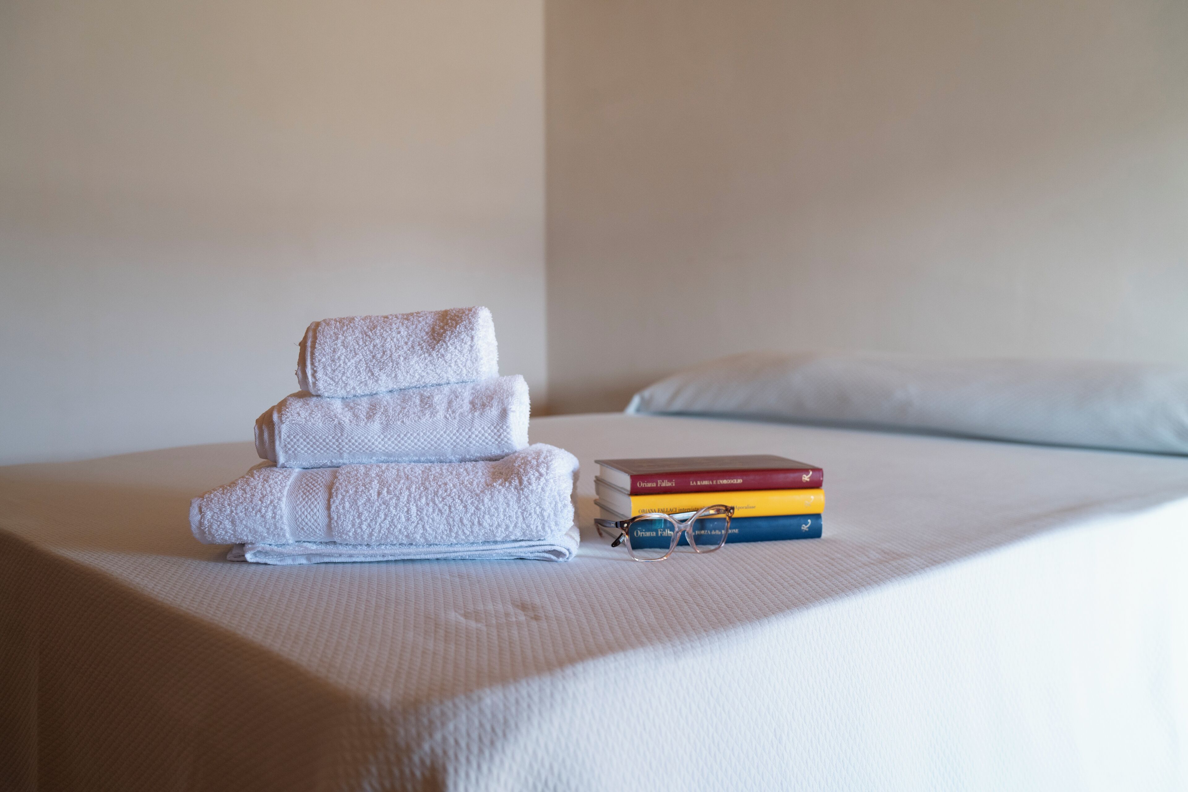 A neatly made bed with a stack of folded towels and a few books on the bed.