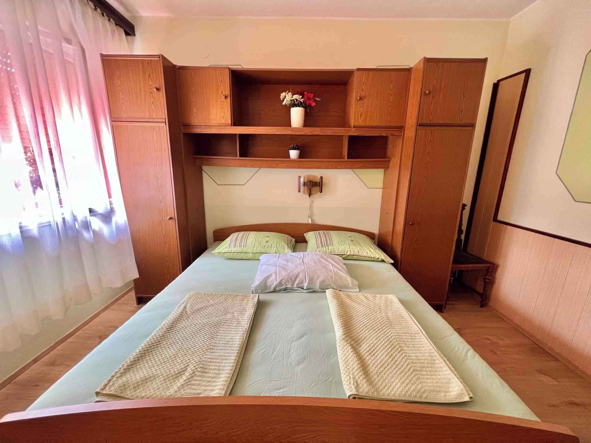 A bedroom with a bed, wooden wardrobe, and a small shelf with a vase.