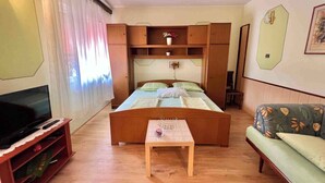 A room with a bed, a TV, a wooden table, a sofa, and a wall-mounted shelf with a vase. - Studio with air conditioning and with terrace (Dramalj)