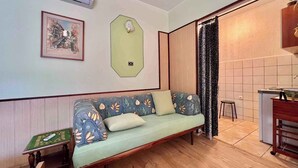A cozy room with a sofa, a small table, an air conditioning unit, a framed picture, a green wall-mounted light switch, and a kitchen area with a sink and countertop. - Studio with air conditioning and with terrace (Dramalj)