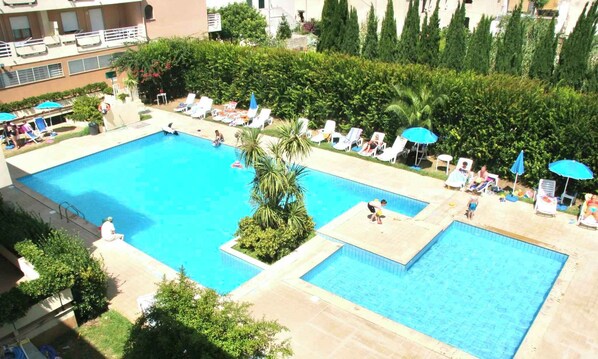 Una piscina rectangular grande con varias pistas, rodeada de tumbonas y sombrillas.