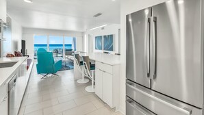 A modern kitchen with a large stainless steel refrigerator, white cabinetry, and a view of the ocean. - Beach House 104A - Gulf Front Resort! (Miramar Beach)
