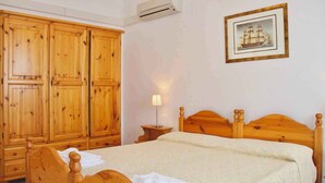 Une chambre à coucher avec un lit en bois, une armoire en bois, une table de chevet avec une lampe et un tableau encadré au mur.