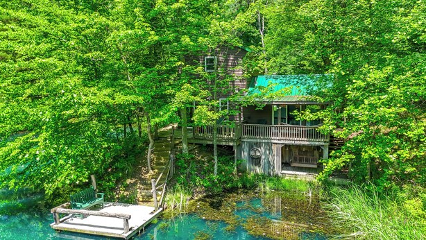 Une cabane en bois dotée d’un balcon, entourée d’une forêt dense et bordée d’un plan d’eau aux eaux claires.