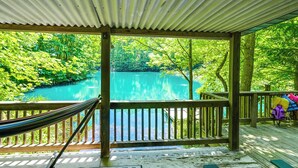 Une terrasse en bois avec un hamac, donnant sur un lac turquoise bordé d’une végétation luxuriante.