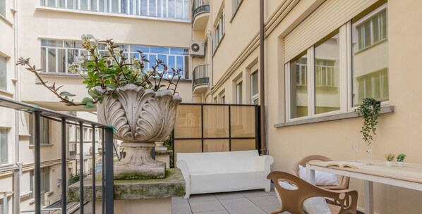 A balcony with a white sofa, a table with two glasses, and a potted plant.