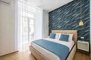 Ein Schlafzimmer mit Bett, Nachttisch, einer Wand mit Wellenmuster, einer Pendelleuchte und einem Fenster mit Vorhängen.
