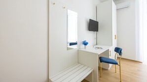Una habitación moderna y minimalista con un escritorio blanco, una silla azul, un banco y un televisor de pantalla plana montado en la pared.