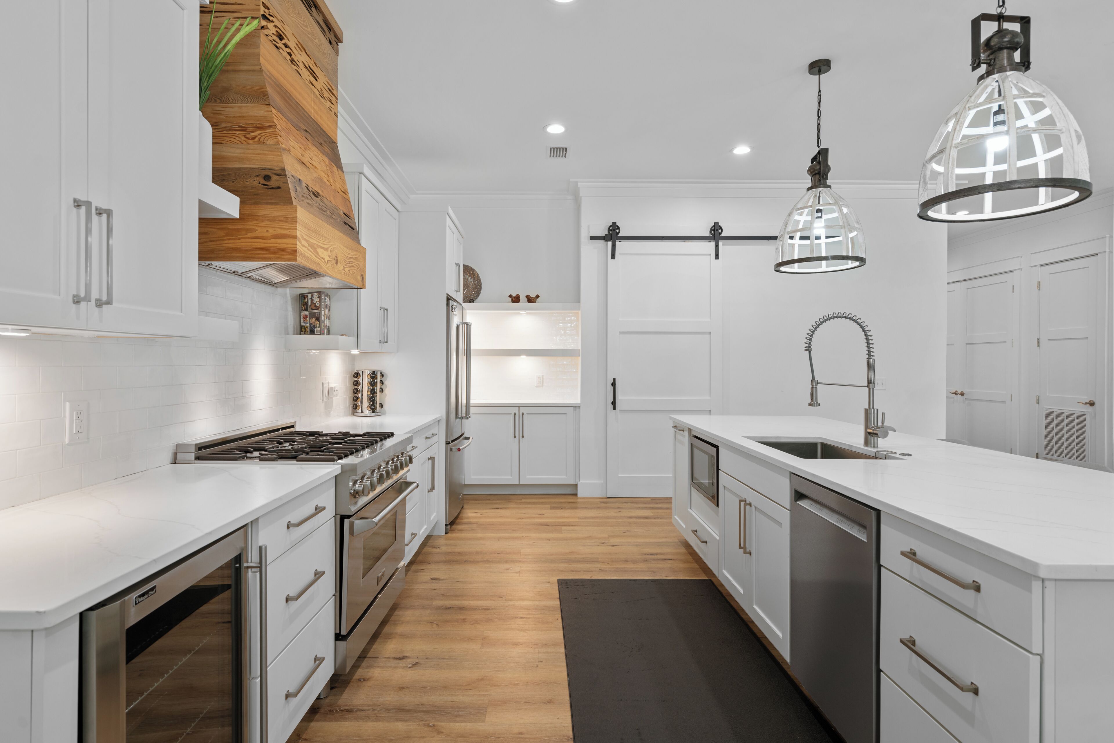Una cocina moderna con armarios blancos, electrodomésticos de acero inoxidable y una pared decorativa de madera.