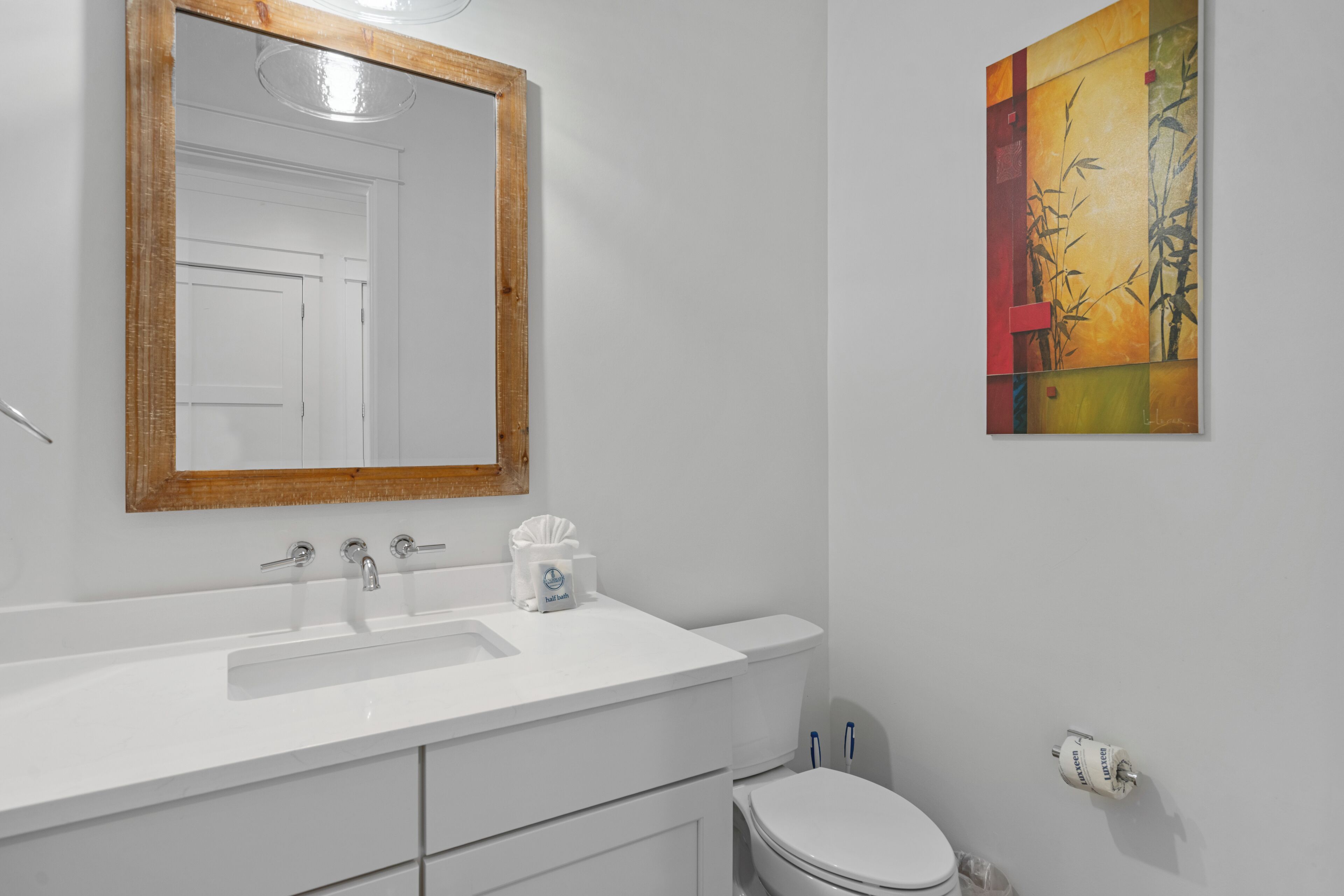 A bathroom with a white sink, a mirror with a wooden frame, a toilet, and a wall-mounted toilet paper holder.