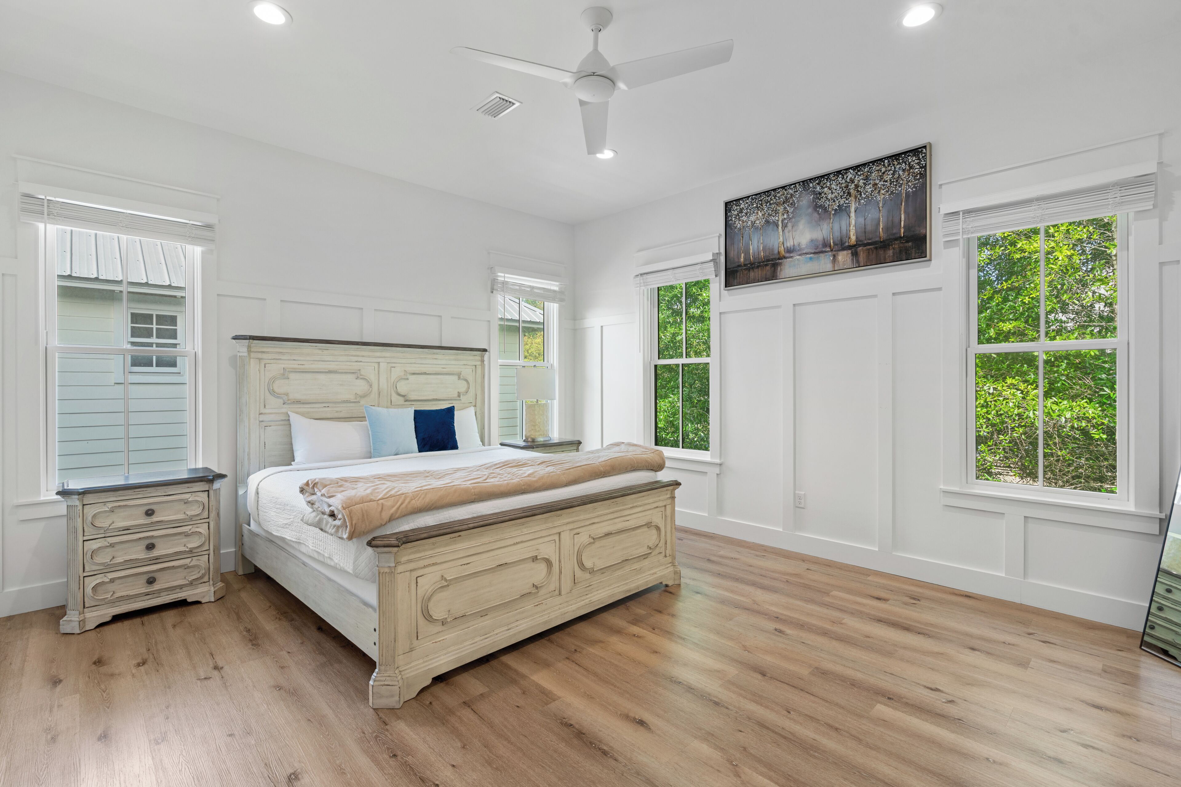 A bedroom with a bed, a nightstand, a ceiling fan, and large windows.