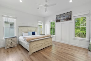 Quarto com cama, mesa de cabeceira, ventilador de teto e janelas amplas.