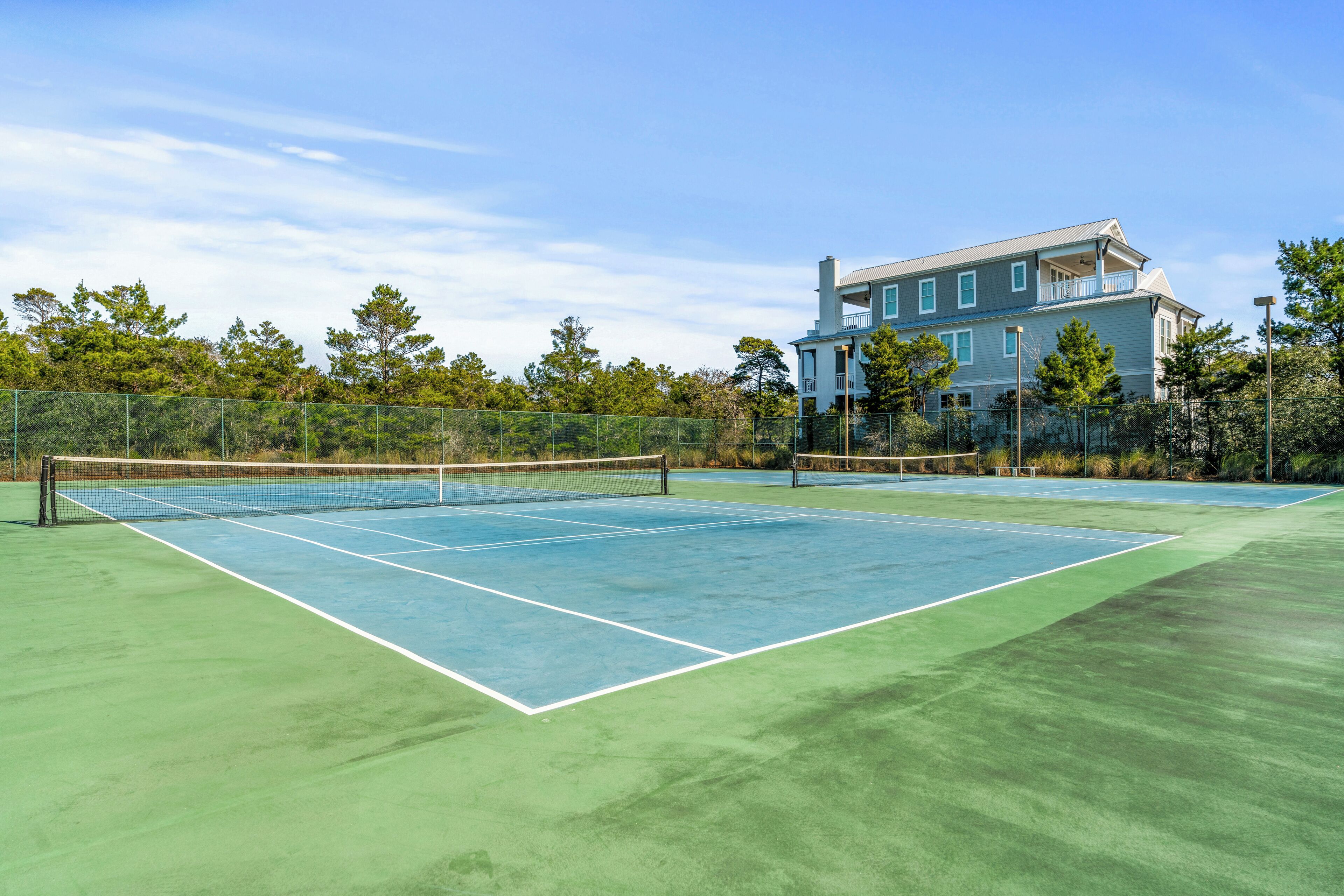 A tennis court with a net, surrounded by a fence, and a large building in the background.