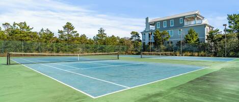 A tennis court with a net, surrounded by a fence, and a large building in the background.