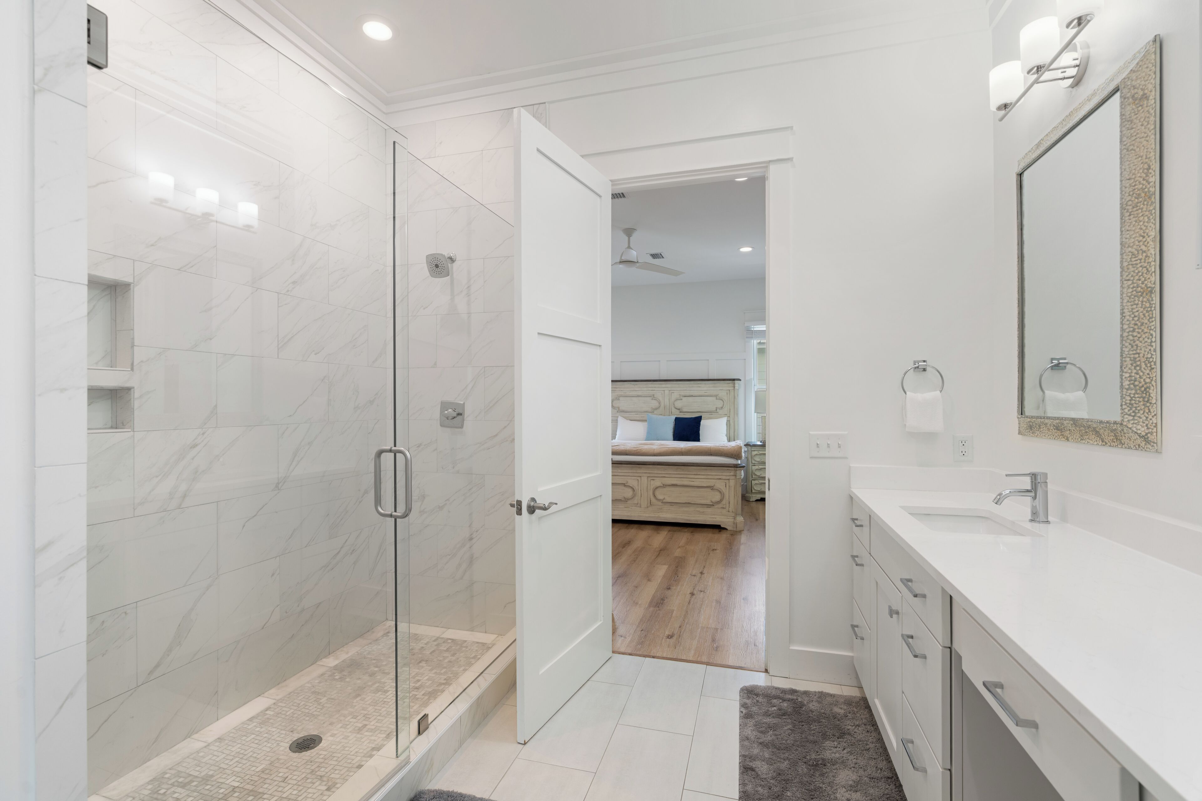 A modern bathroom with a glass-enclosed shower, white marble tiles, a double sink vanity, and a large mirror.