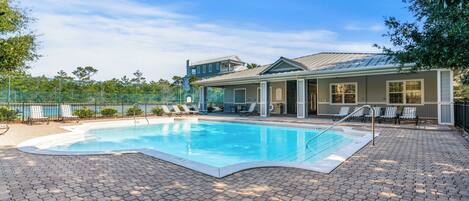A swimming pool with lounge chairs, a covered patio, and a view of a building with a metal roof.
