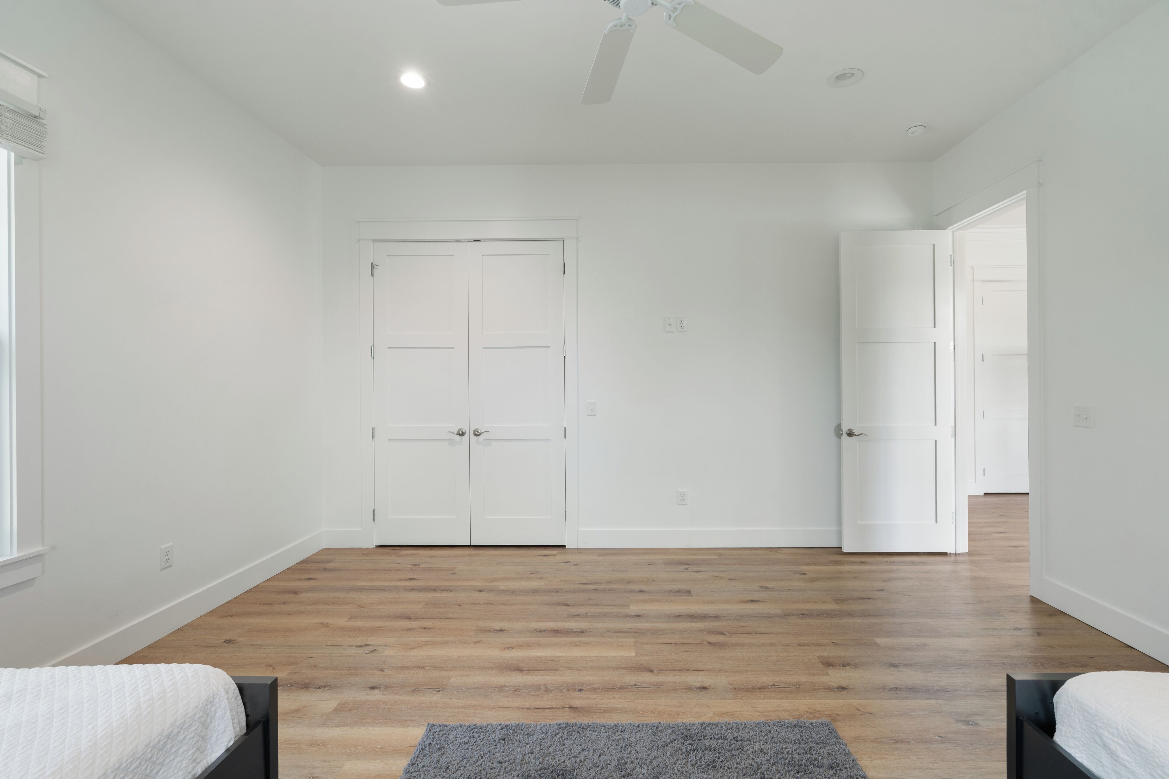 A room with a wooden floor, two beds, a ceiling fan, and white doors.