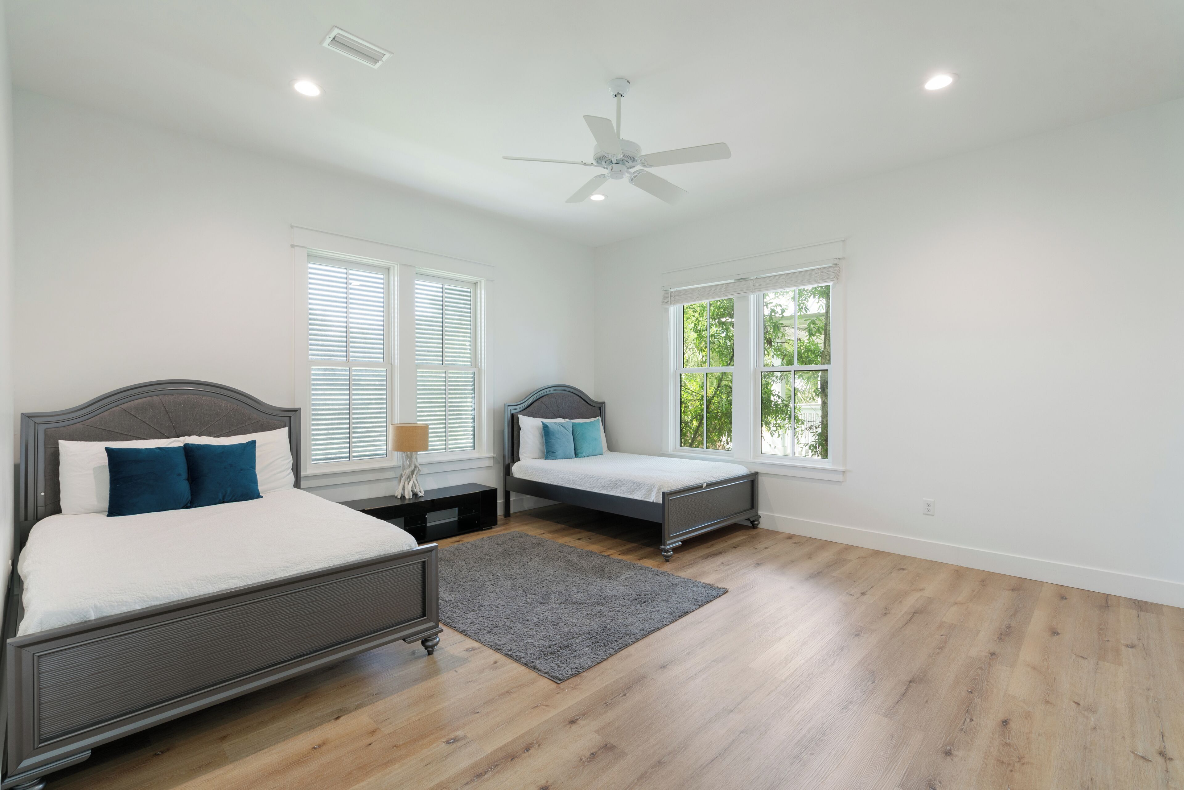 A bedroom with two beds, a ceiling fan, and large windows.