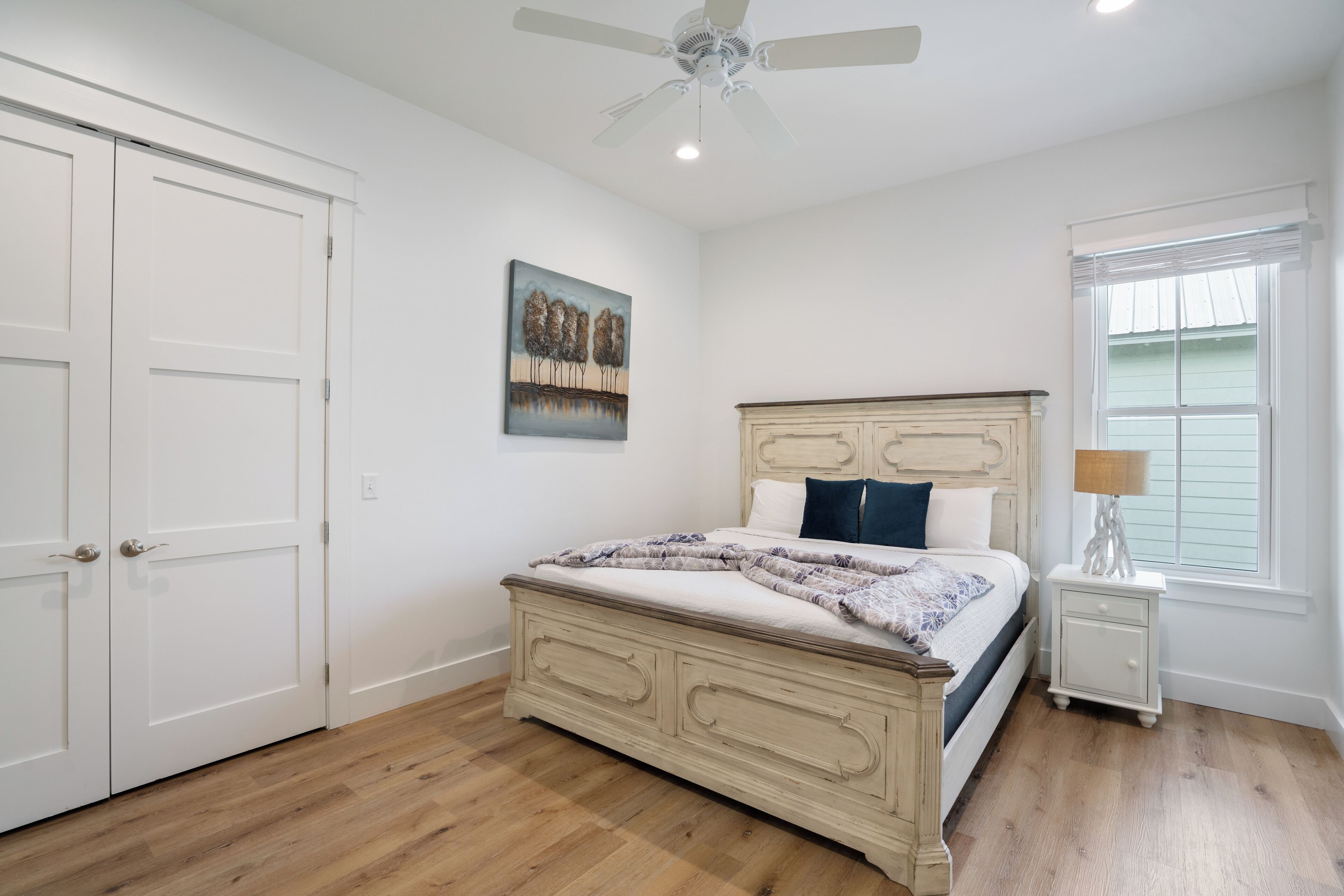 A bedroom with a bed, nightstand, ceiling fan, and a painting on the wall.