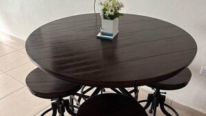A round dining table with four chairs, a small white vase with flowers, and a power cord.