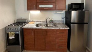 A compact kitchen with wooden cabinets, a stainless steel refrigerator, a microwave, a gas stove, and a sink.